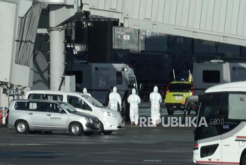 Petugas mengenakan pakaian pelindung berada di sekitar pesawat yang mendarat membawa warga Jepang dari Wuhan di Bandara Haneda, Tokyo, Jepang, Rabu (29/1). Sejumlah maskapai menangguhkan penerbangan ke sejumlah kota di China.