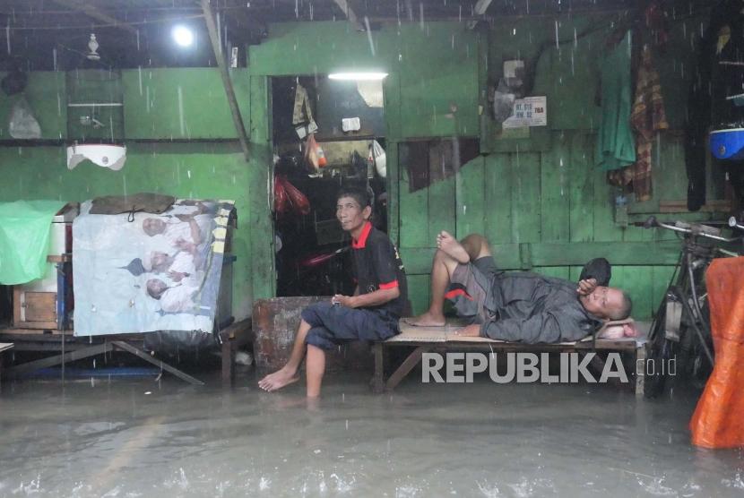 Warga  nampak berbaring dan duduk di depan kiosnya yang terendam banjir  di sekitar Sunter Jaya Jakarta, Sabtu (8/2).