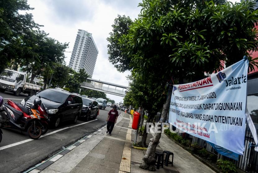 Warga melintas di dekat spanduk sosialisasi parkir ganjil genap di Jalan Gajah Mada, Jakarta. Jalan Gajah Mada jadi pelanggaran terbanyak saat sosialisasi ganjil-genap di Jakbar.