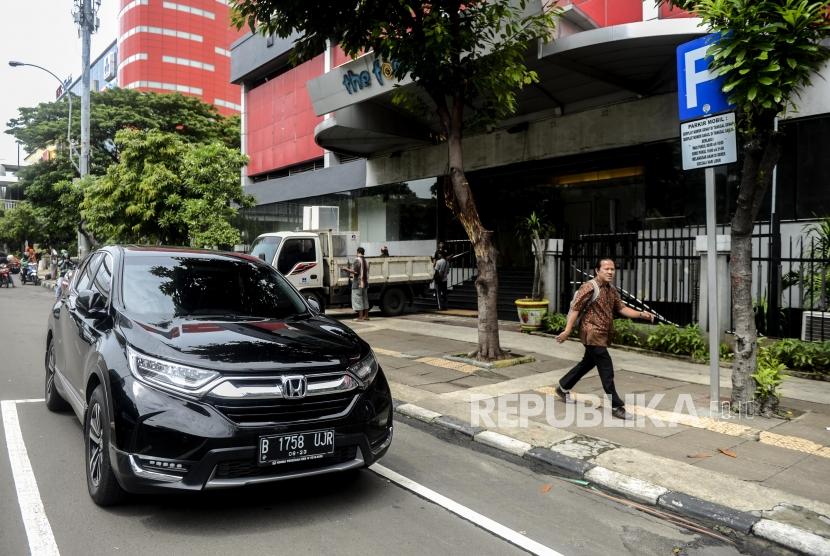 Warga melintas di dekat mobil yang terparkir di Jalan Gajah Mada, Jakarta, Kamis (20/2).
