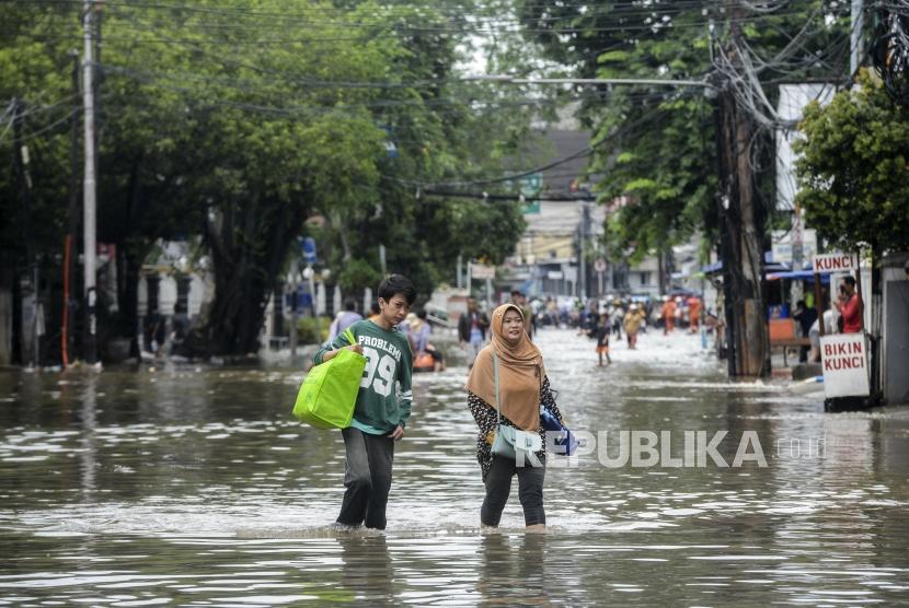 Warga melintasi genangan air saat terjadi banjir di kawasan Bendungan Hilir, Jakarta, Selasa (25/2). Banjir telah menyebabkan banyak sektor lumpuh, seperti peti kemas karena lumpuhnya jalan dari depo ke pelabuhan dan sebaliknya.