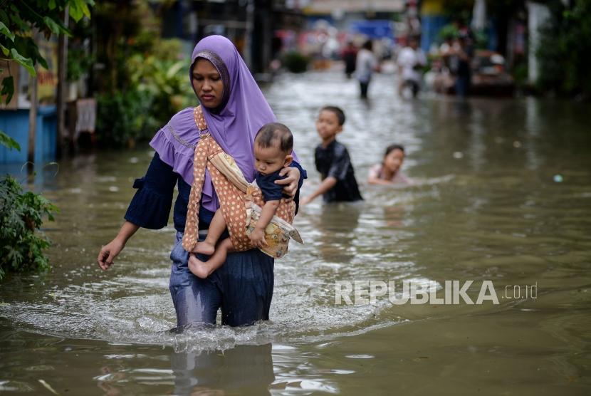 Warga berjalan melintasi area yang terendam banjir di Jalan Satria IV, Kelurahan Jelambar, Jakarta Barat, Selasa (25/2).
