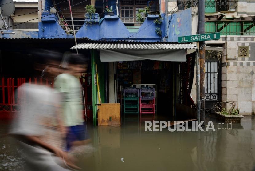 Warga berjalan melintasi area yang terendam banjir di Jalan Satria IV, Kelurahan Jelambar, Jakarta Barat, Selasa (25/2).