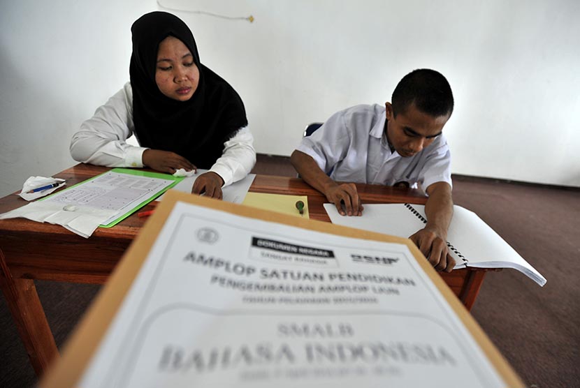 Siswa penyandang disabilitas netra membaca soal dalam bentuk braille di samping pendampingnya saat mengikuti ujian nasional (UN) di SLBA Yapti Makassar, Sulawesi Selatan, Senin (4/4).  (Antara/Yusran Uccang)