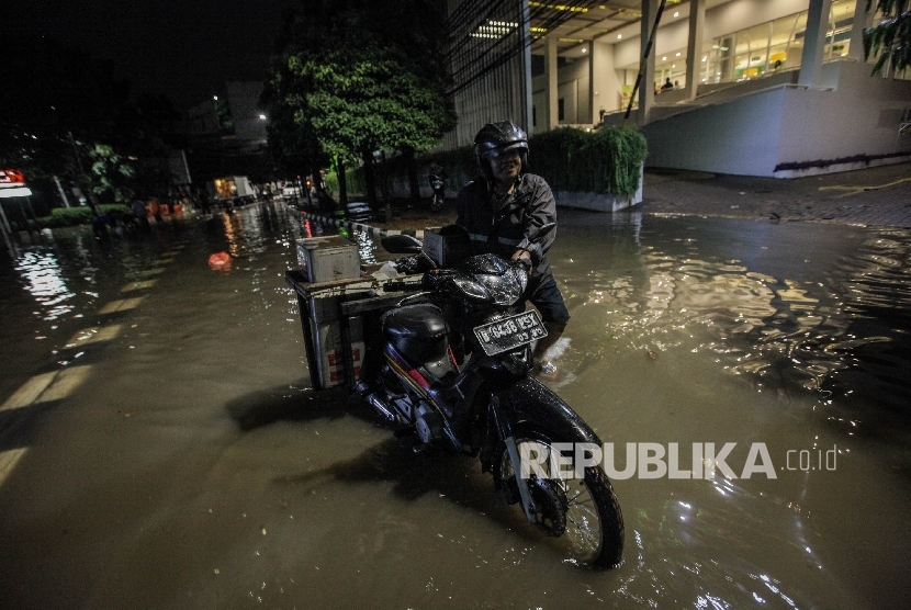 Pengendara sepeda motor melintasi genangan banjir di kawasan niaga Kemang, Ahad malam (25/9).