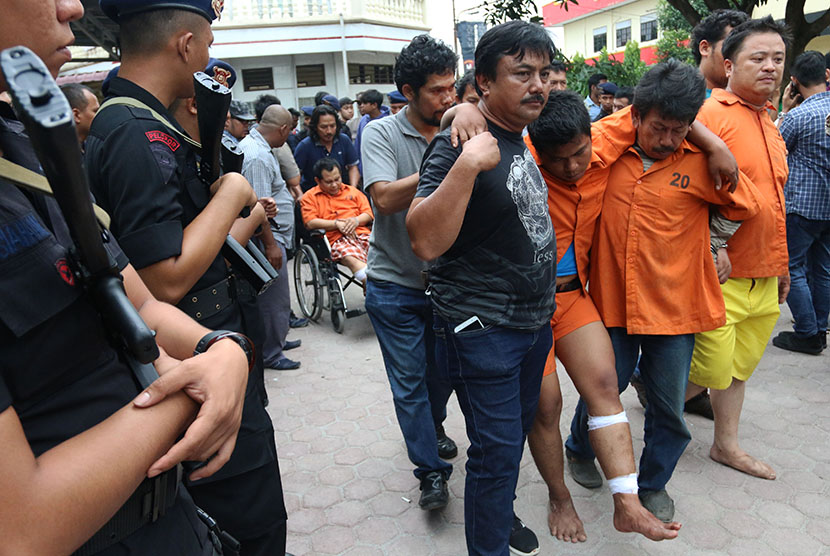 Polisi berpakaian sipil menggiring tersangka penembakan pemilik toko airsoft gun pada gelar kasus, di Medan, Sumatera Utara, Ahad (22/1).