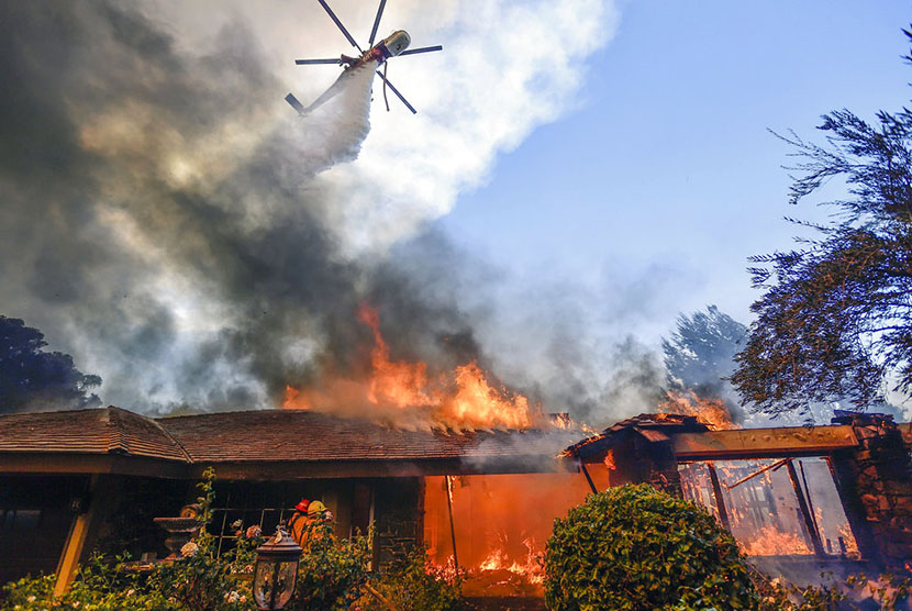 Sebuah helikopter berupaya memadakan api akibat kebakaran dahsyat yang melanda California, Senin (9/10).