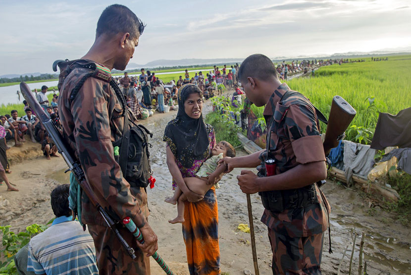  Tentara Bangladesh memeriksa seorang pengungsi Muslim Rohingya yang menggendong anaknya yang sakit, sebelum mengizinkannya masuk menuju kamp pengungsian di Palong Khali, Bangladesh.