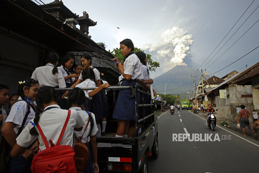  Pelajar berangkat ke sekolah dengan latar pemandangan Gunung Agung saat memuntahkan asap dan abu vulkanis di Karangasem, Bali, Selasa (28/11).  