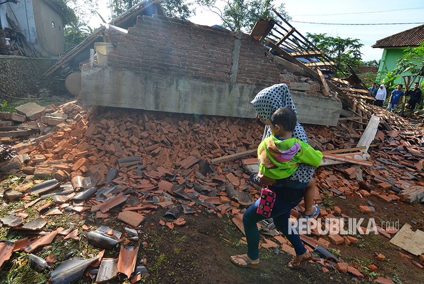 Warrga melintas di depan rumah permanen berlantai dua yang ambruk akibat gempa bumi di Desa Gunung Sari, Jawa Barat, Sabtu (16/12). 
