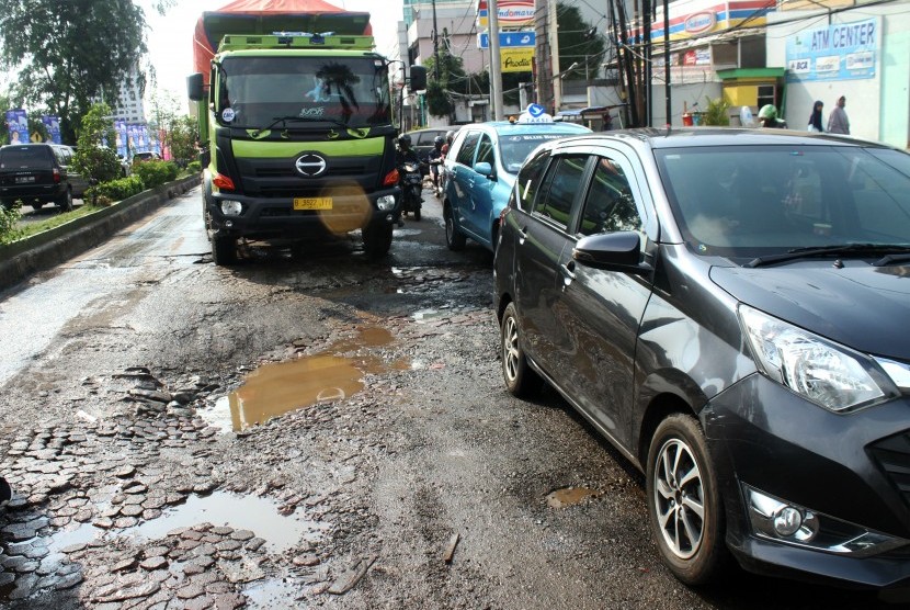 Pengendara truk memperlambat laju kendaraannya saat melintas jalan rusak di Jalan KH Noer Ali, Kalimalang, Bekasi, Jawa Barat, Selasa (27/11/2018). 