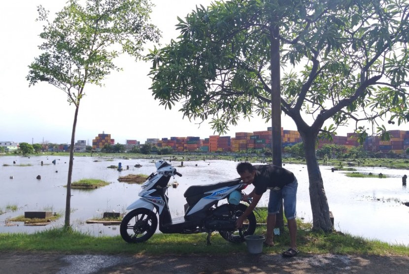 Seorang warga Gang Lengkong mencuci sepeda motor di Tempat Pemakaman Umum (TPU) Semper, Cilincing, Jakarta Utara yang terendam banjir, Kamis (6/12).