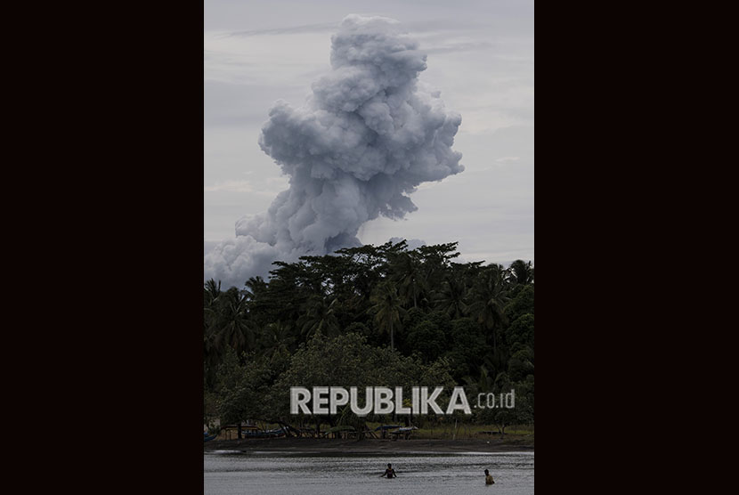 Warga beraktivitas dengan latar belakang erupsi Gunung Anak Krakatau di Pelabuhan Pulau Sebesi, Lampung Selatan, Lampung.