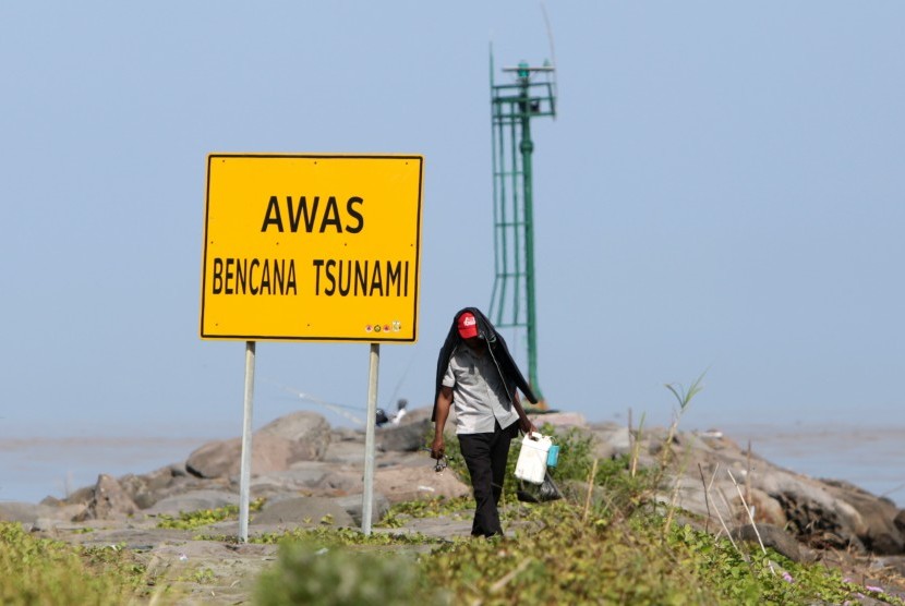Warga berjalan di dekat rambu peringatan bencana tsunami di pantai wisata Kampung Jawa, Banda Aceh, Aceh, Selasa (8/1/2019).