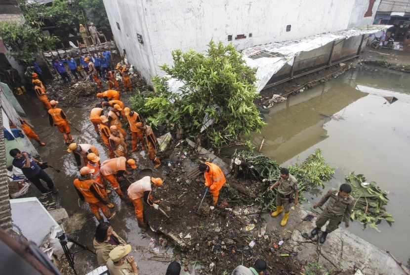 Petugas PPSU membersihkan lumpur yang menggenangi jalan pemukiman warga karena tanggul aliran Kali Pulo jebol di Kelurahan Jati Padang, Kecamatan Pasar Minggu, Jakarta, Senin (14/1/2019).