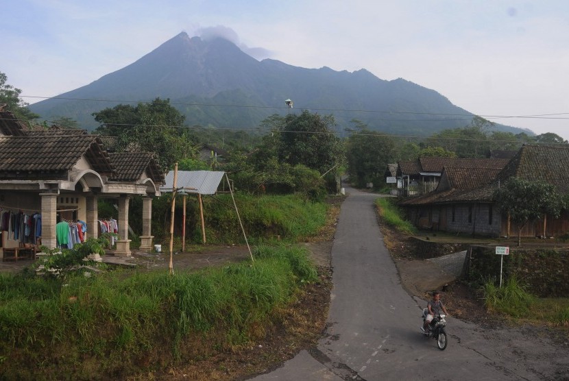 Warga melintas di jalan desa dengan berlatar belakang Gunung Merapi. 