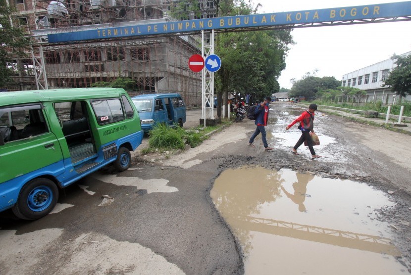 Penumpang melewati kubangan air di jalan yang rusak di Terminal Bubulak, Kota Bogor, Jawa Barat, Jumat (15/2/2019).