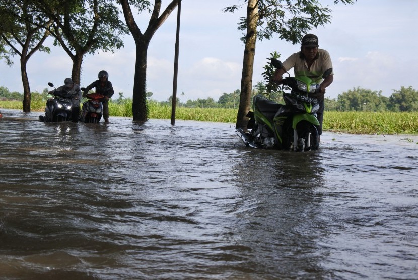 Warga mendorong motor yang mogok saat melintasi banjir di Desa Glundengan, Wuluhan, Jember, Jawa Timur