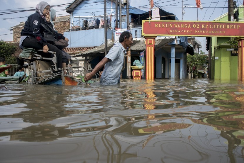 Warga menggunakan becak untuk melintasi banjir luapan Sungai Citarum di kawasan Dayeuhkolot, Kabupaten Bandung, Jawa Barat, Selasa (9/4/2019).