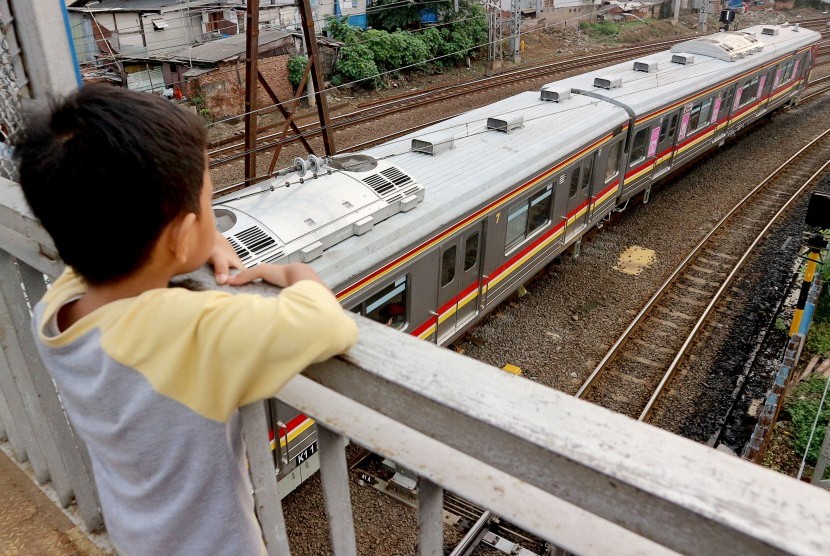 Seorang bocah mengamati rangkaian kereta rel listrik (KRL) Commuterline melintas di kawasan Stasiun Jatinegara, Jakarta, Selasa (9/4/2019).