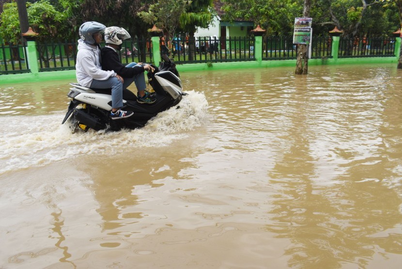 Pelajar mengendarai sepeda motor melintasi jalan yang terendam banjir di Kabupaten Madiun, Jawa Timur, Senin (29/4/2019).