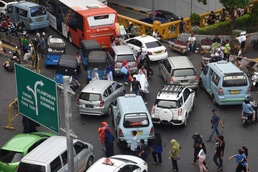 Warga dan kuli angkut menyeberang jalan di antara kendaraan bermotor yang terjebak kemacetan di kawasan Pasar Tanah Abang, Jakarta, Rabu (15/5/2019). 