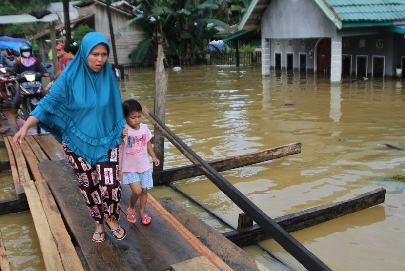 Warga melintasi jembatan darurat yang baru dibuat akibat terus naiknya ketinggian banjir di Kelurahan Sampara, Konawe, Sulawesi Tenggara, Jumat (14/6/2019).