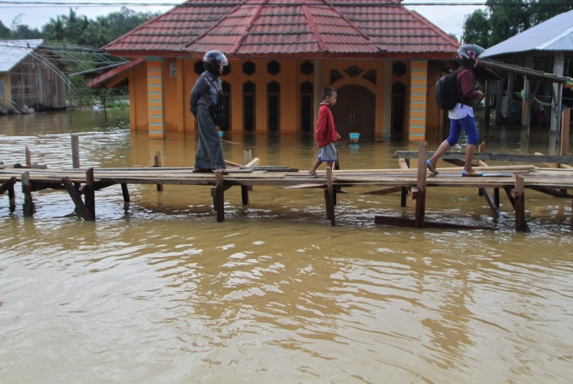 Warga melintasi jembatan darurat yang baru dibuat akibat terus naiknya ketinggian banjir di Kelurahan Sampara, Konawe, Sulawesi Tenggara, Jumat (14/6/2019).