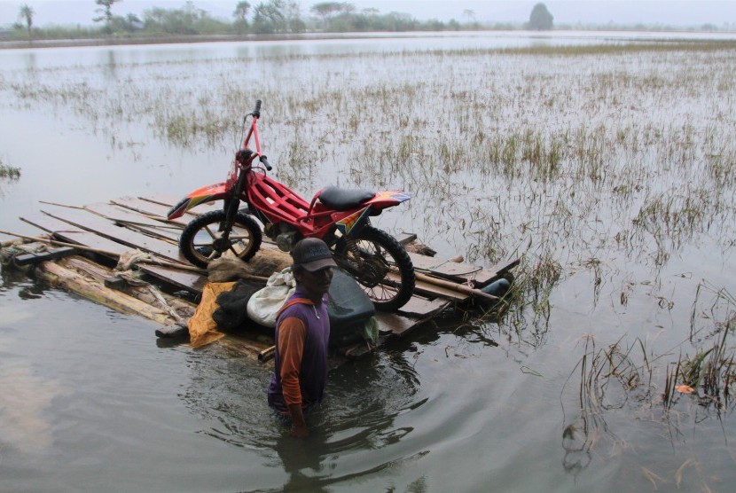 Seorang petani membawa sepeda motornya dengan rakit melintasi banjir yang merendam sawah di Desa Puduria, Konawe, Sulawesi Tenggara, Rabu (19/6/2019).