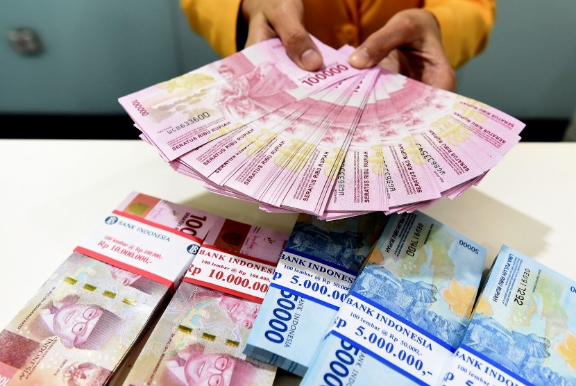 Seorang teller Bank Mandiri menunjukkan uang pecahan Rp100.000 dan Rp50.000 di Plasa Mandiri, Jakarta, Senin (8/7/2019).