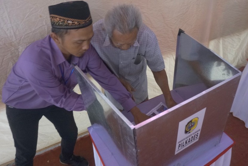 Petugas membantu warga menggunakan hak pilih dalam Pemilihan Kepala Desa (Pilkades).
