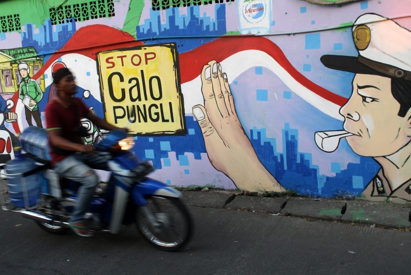 Warga melintas di dekat dinding lukisan mural bertuliskan imbauan stop calo pungutan liar di Kantor Pelayanan SIM Mapolres Metro Bekasi Kota, di Bekasi, Jawa Barat, Rabu (24/7/2019). 