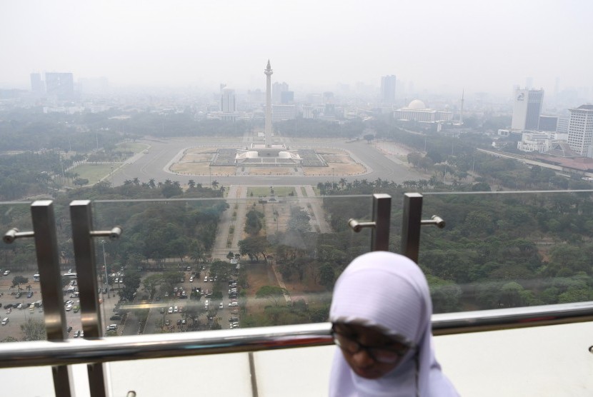 Warga beraktivitas dengan latar belakang suasana gedung bertingkat yang diselimuti asap polusi di Jakarta, Senin (29/7/2019).