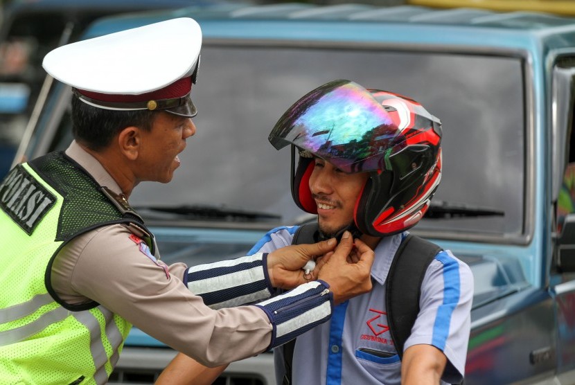 Ilustrasi tertib lalu lintas. Foto: Polantas membantu mengencangkan tali helm pengendara sepeda motor saat dilakukan kampanye 
