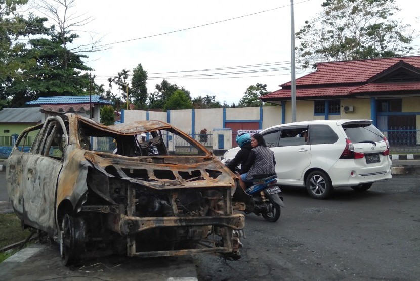 Warga melintas di samping bangkai mobil yang terbakar di Manokwari, Papua Barat, Selasa (20/8/2019).