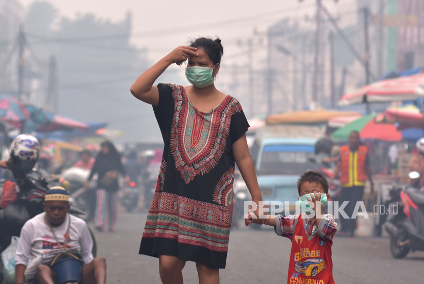 Seorang ibu dan anaknya mengenakan masker medis saat asap kebakaran hutan dan lahan (Karhutla) menyelimuti Kota Pekanbaru, Riau, Selasa (10/9/2019