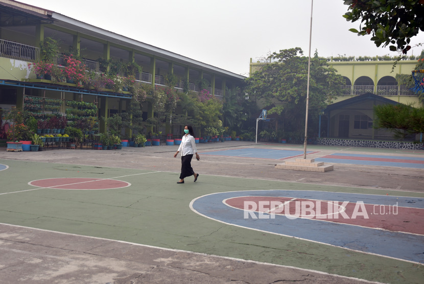 Seorang guru mengenakan masker melintasi halaman SD Santa Maria yang kosong karena sekolah diliburkan di Kota Pekanbaru, Riau, Rabu (11/9/2019). 