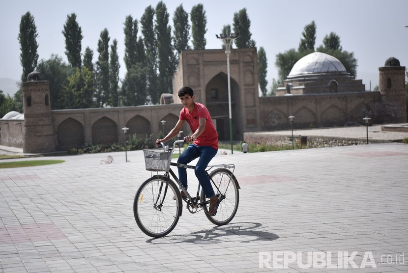 Seorang warga bersepeda melintas di depan bangunan madrasah di komplek kota tua Hisor (Hissar), Tajikistan. Mal, restoran, hotel, dan sektor jasa di Tajikistan akan beroperasi kembali. Ilustrasi. 