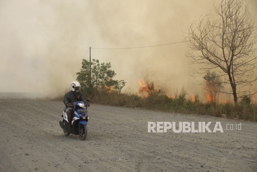 Pengendara roda dua melintas di samping api yang membakar lahan gambut di Jalan Tegal Arum kawasan Syamsudin Noor, Banjarbaru, Kalimantan Selatan, Jumat (13/9/2019).