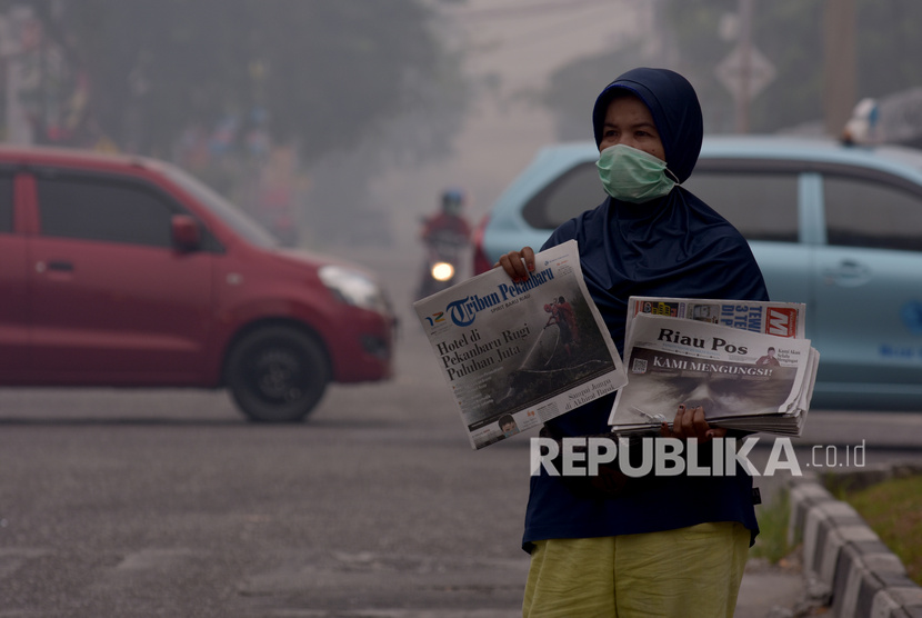 Seorang penjual koran mengenakan masker medis saat berjualan di tengah asap kebakaran hutan dan lahan (Karhutla) yang makin pekat menyelimuti Kota Pekanbaru, Riau, Jumat (13/9/2019). 