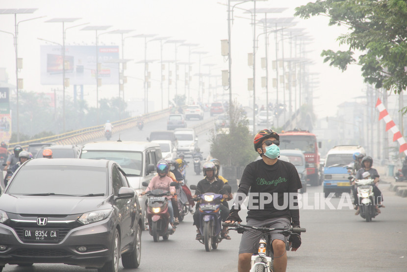 Warga bersepeda menggunakan masker pelindung pernapasan ketika melintas di jalan Ahmad Yani yang terpapar kabut asap di Banjarmasin, Kalimantan Selatan, Ahad (15/9/2019).