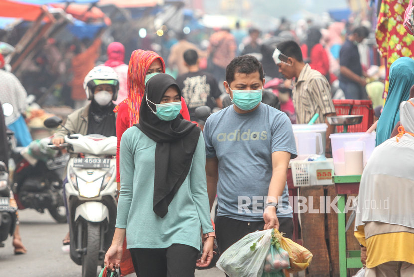 Warga beraktivitas mengenakan masker medis ketika kabut asap Karhutla menyelimuti Kota Pekanbaru, Riau, Ahad (15/9/2019).