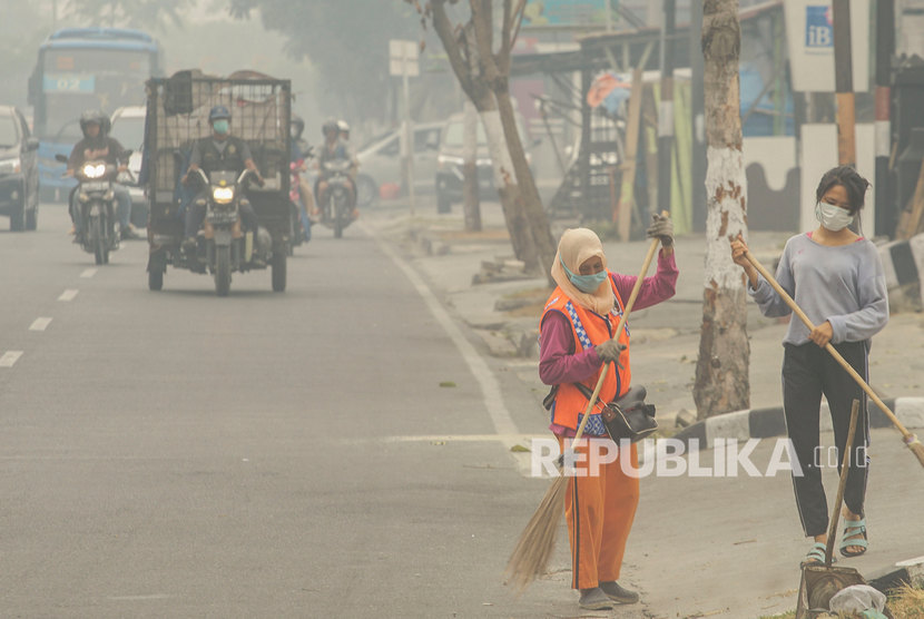Petugas Kebersihan mengenakan masker ketika menyapu jalan saat kabut asap dampak kebakaran hutan dan lahan menyelimuti Kota Pekanbaru, Riau.