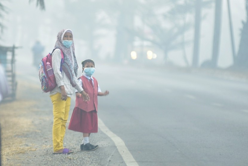 Seorang siswa bersama orang tuanya mengenakan masker saat menunggu angkutan umum, di Palembang, Sumatra Selatan.