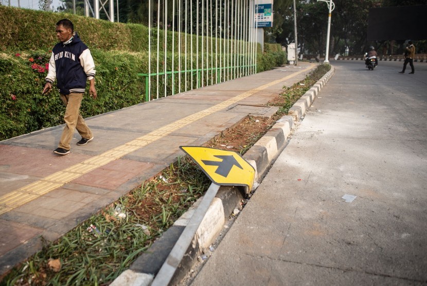 Warga berjalan di dekat rambu lalu lintas yang rusak pascaunjuk rasa mahasiswa di Jalan Gatot Subroto, Slipi, Jakarta, Rabu (25/9/2019). 