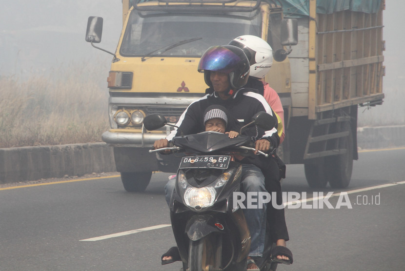 Pengendara motor melintas di jalan lingkar selatan yang diselimuti kabut asap.