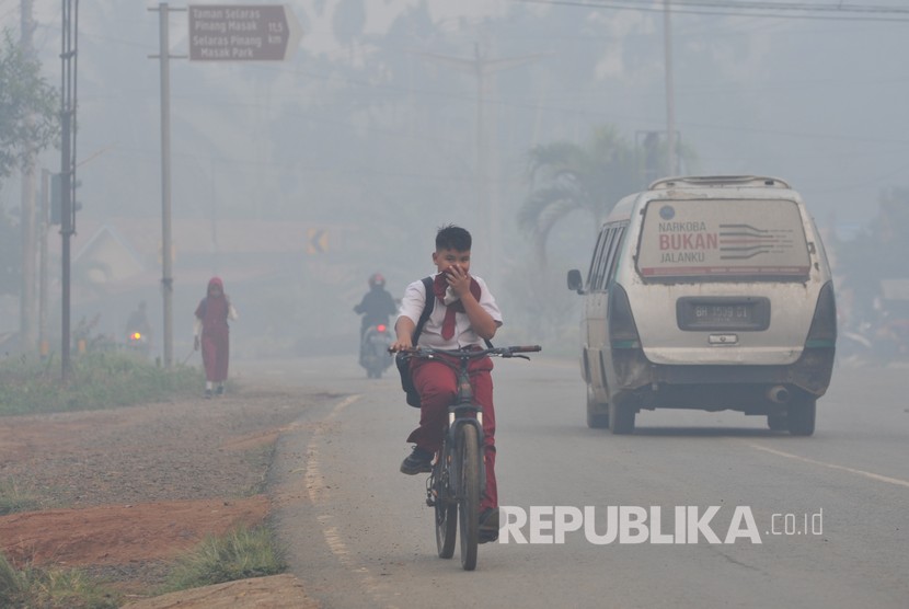 Pelajar SDN 61 Kabupaten Tanjungjabung Timur dan warga beraktivitas di Jalan Lintas Jambi-Muara Sabak yang diselimuti kabut asap karhutla di Muara Sabak Barat, Tanjungjabung Timur, Jambi.
