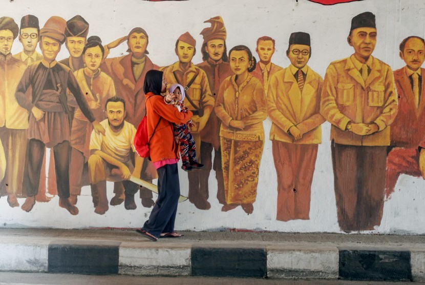 Warga melintas di depan mural bergambar tokoh Pahlawan Nasional di Jalan Raya Situ Cipayung, Jakarta Timur, Ahad (13/10/19). 