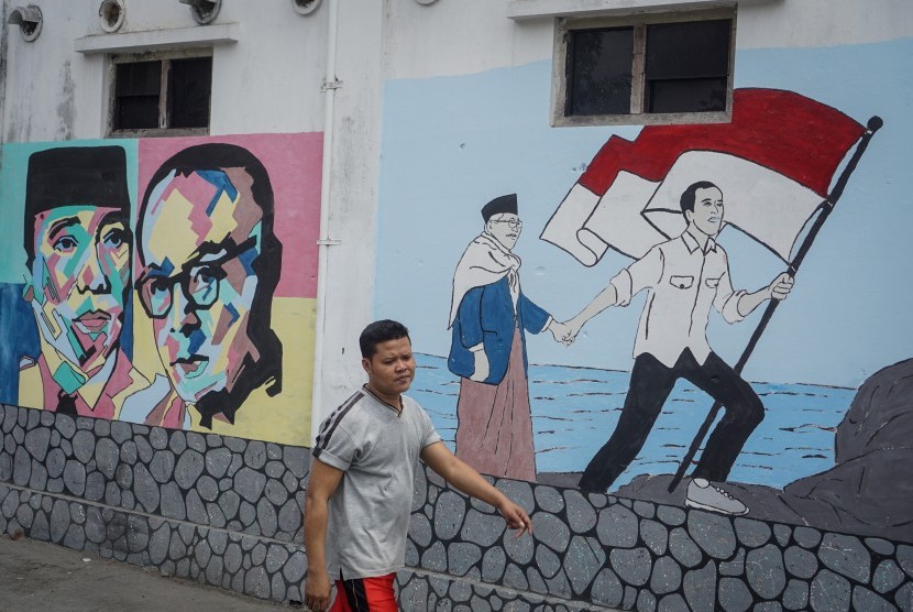 Warga melintas didepan mural bergambar Presiden dan Wakil Presiden terpilih Joko Widodo-Ma'ruf Amin di kampung Punggawan, Banjarsari, Solo, Jawa Tengah, Rabu (16/10/2019).