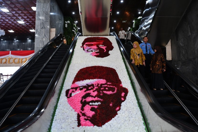Petugas menuruni eskalator di samping hiasan bunga bergambar Presiden dan Wakil Presiden terpilih Joko Widodo dan Ma'ruf Amin disela gladi bersih pelantikan di Kompleks Parlemen, Senayan, Jakarta, Sabtu (19/10/2019).